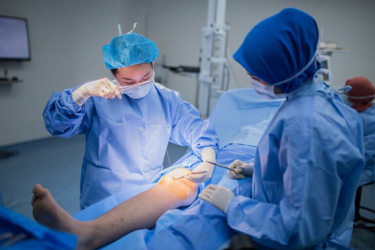 A female doctor is stitching a patient's knee wound after arthroscopic surgery for a torn meniscus.