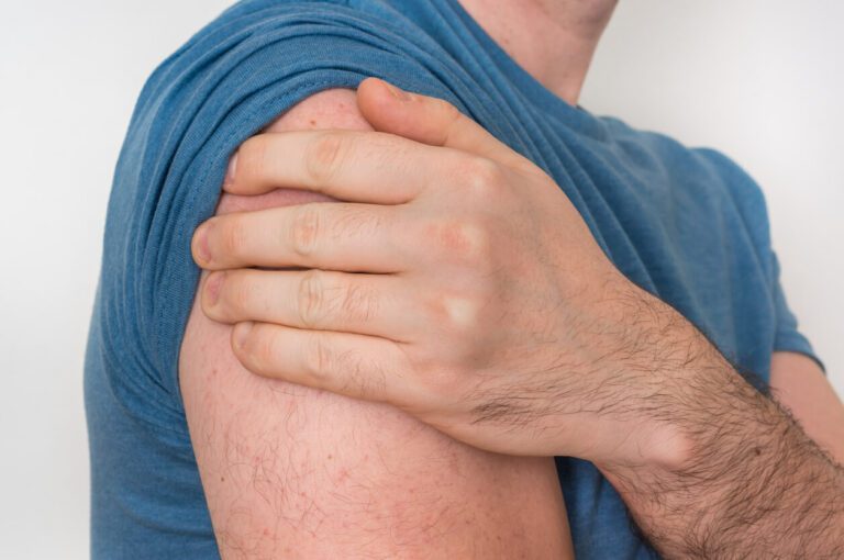 A man is holding his aching arm due to shoulder pain caused by a torn rotator cuff.