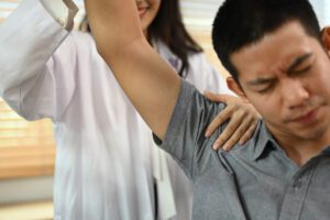 Physical therapist helping male patient doing stretching exercises for rotator cuff tear treatment.
